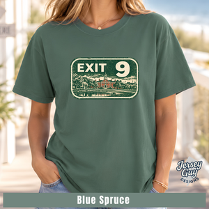 A woman wearing a muted blue-green graphic T-shirt with a vintage-style 'EXIT 9' sign print on the chest. The image includes a 'Jersey Guy Designs' logo and a text banner at the bottom reading 'Blue Spruce'.