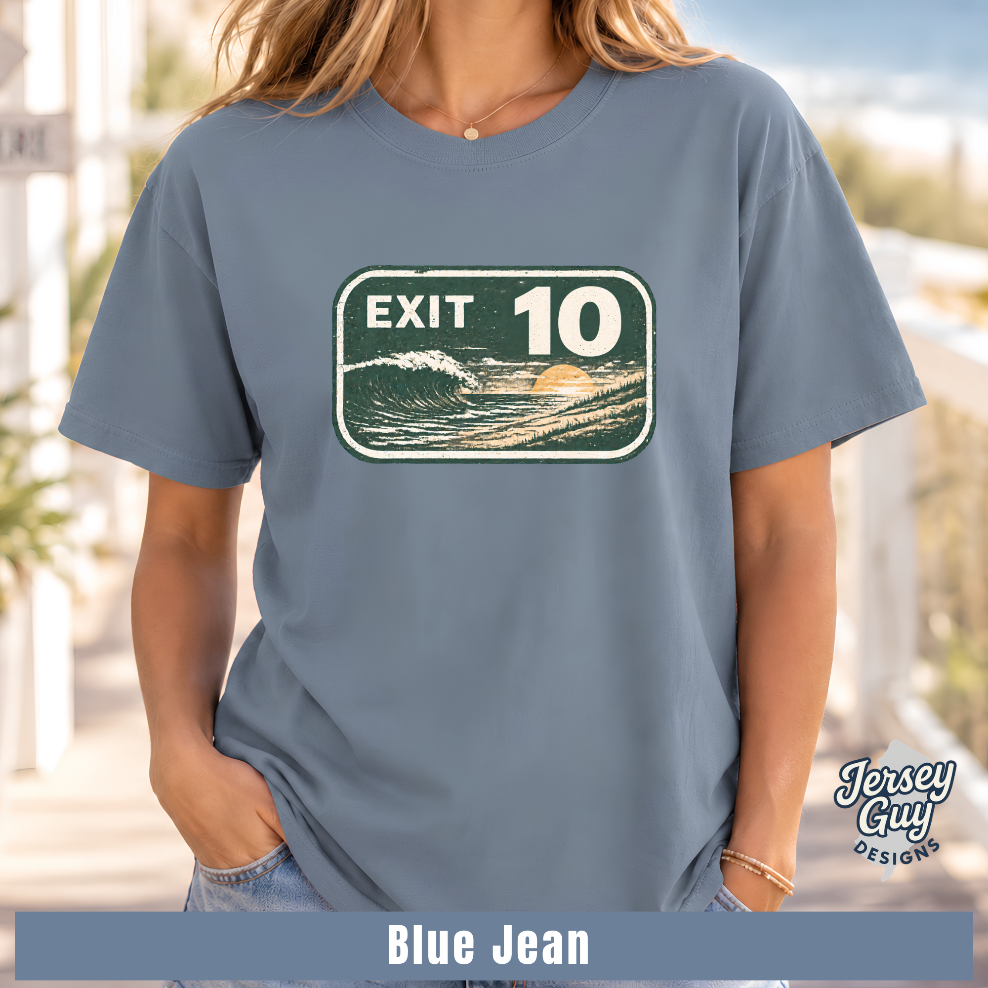 A woman wearing a slate blue graphic t-shirt with a retro 'EXIT 10' wave sign design. The image includes a 'Blue Jean' color label at the bottom and a 'Jersey Guy Designs' logo on the right.